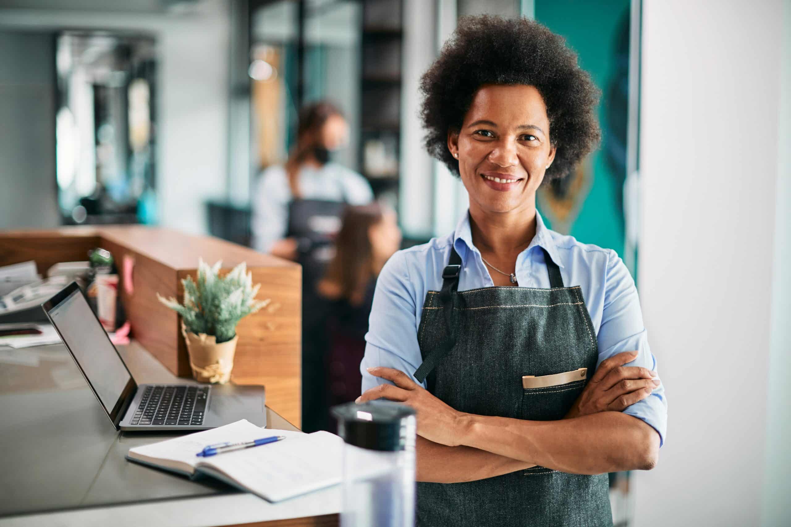 A woman standing confidently at a counter with her laptop and wearing an apron, representing small businesses and franchise agreements in Vancouver