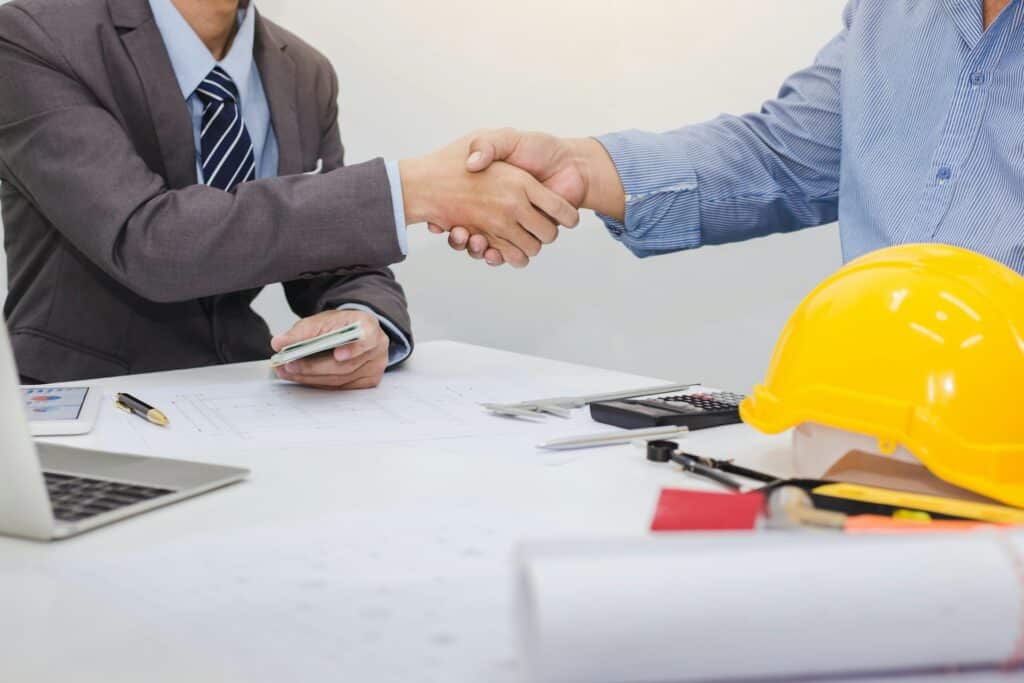 two people shaking hands over a contract with construction gear